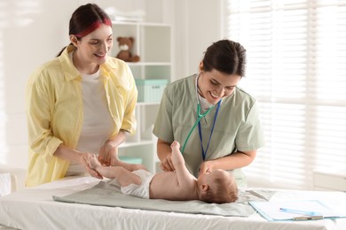 Photo of Mother and her cute little child having appointment with pediatrician in hospital. Doctor examining baby with stethoscope