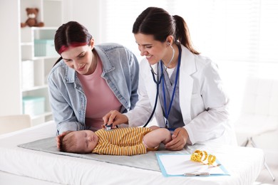 Photo of Mother and her cute little child having appointment with pediatrician in hospital. Doctor examining baby with stethoscope