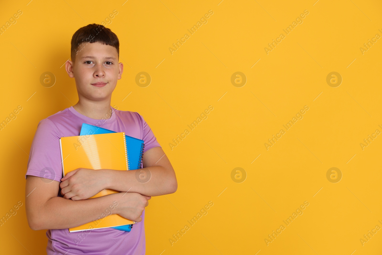 Teenage boy with notebooks on orange background, space for text Photo of Teenage boy with notebooks on orange background, space for text