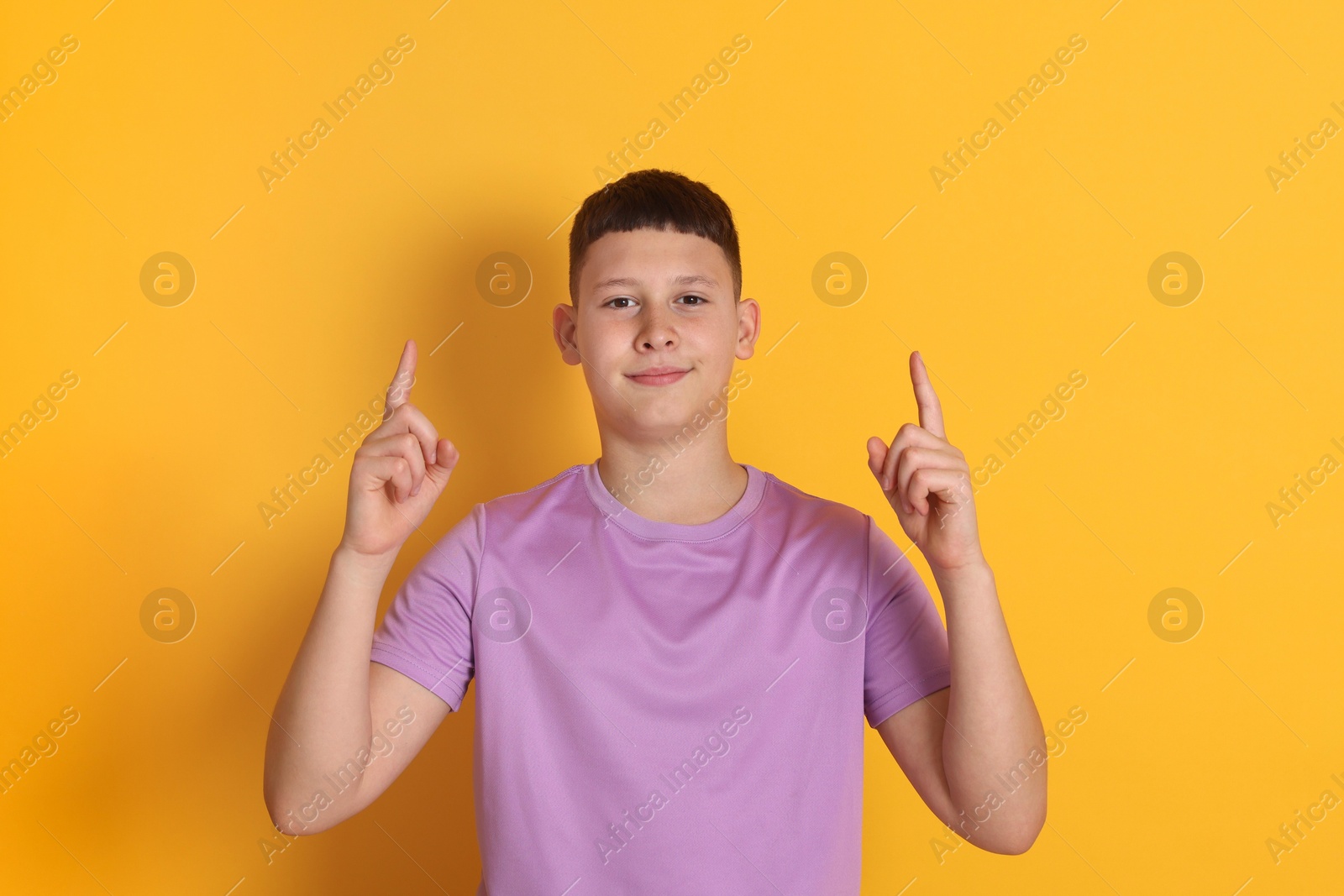 Teenage boy pointing at something on orange background Photo of Teenage boy pointing at something on orange background
