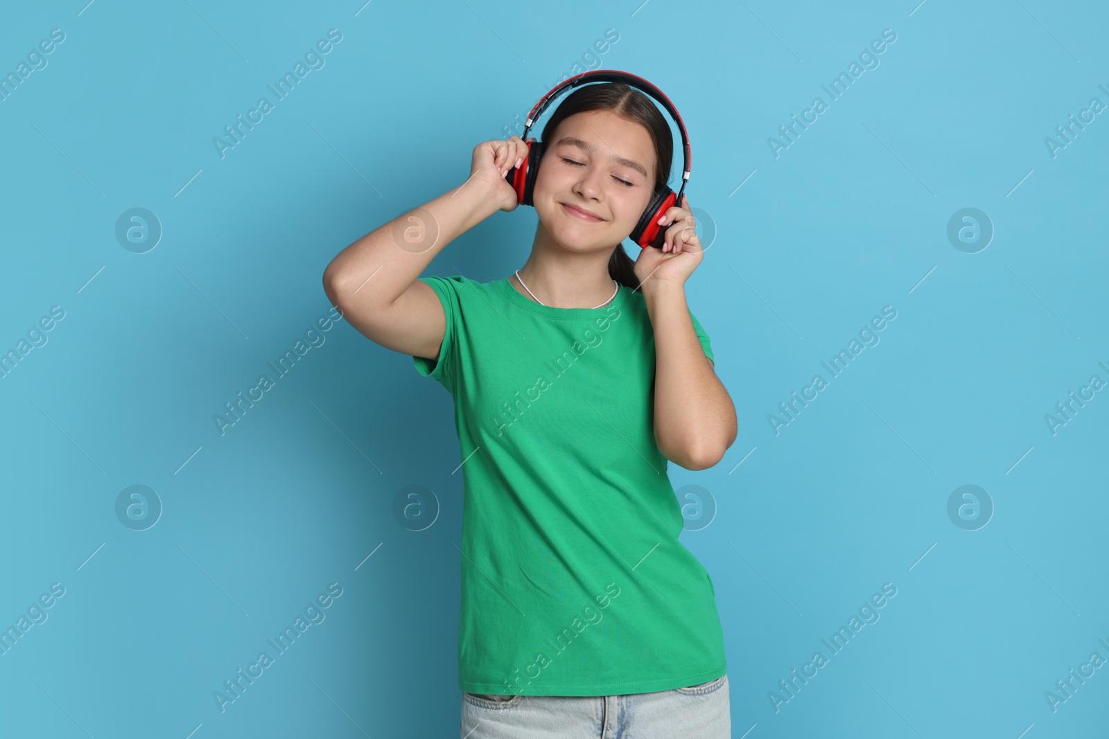 Teenage girl in headphones on light blue background Photo of Teenage girl in headphones on light blue background