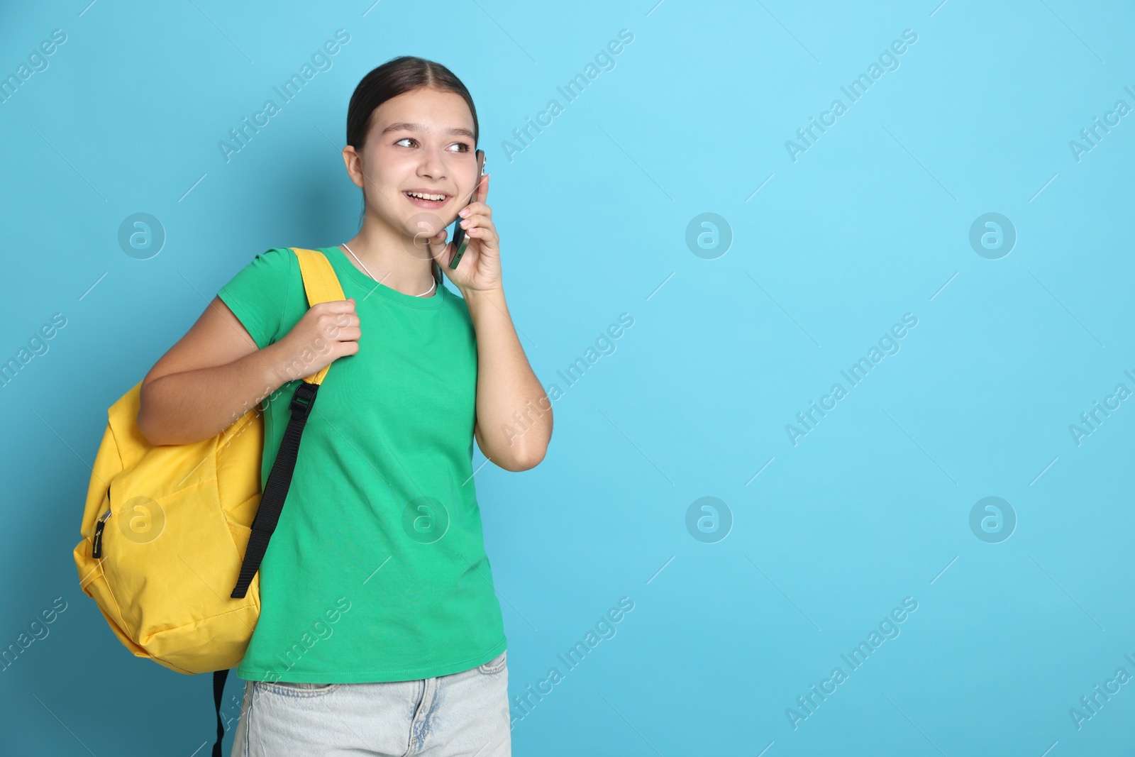 Teenage girl with backpack talking on smartphone against light blue background, space for text Photo of Teenage girl with backpack talking on smartphone against light blue background, space for text