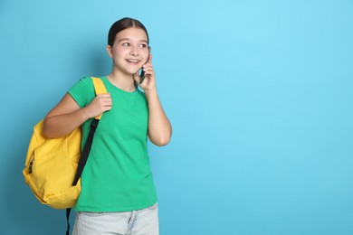 Photo of Teenage girl with backpack talking on smartphone against light blue background, space for text