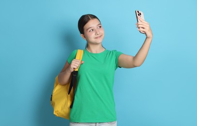 Photo of Teenage girl with backpack taking selfie on light blue background