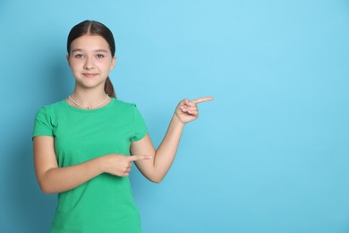 Photo of Teenage girl pointing at something on light blue background, space for text