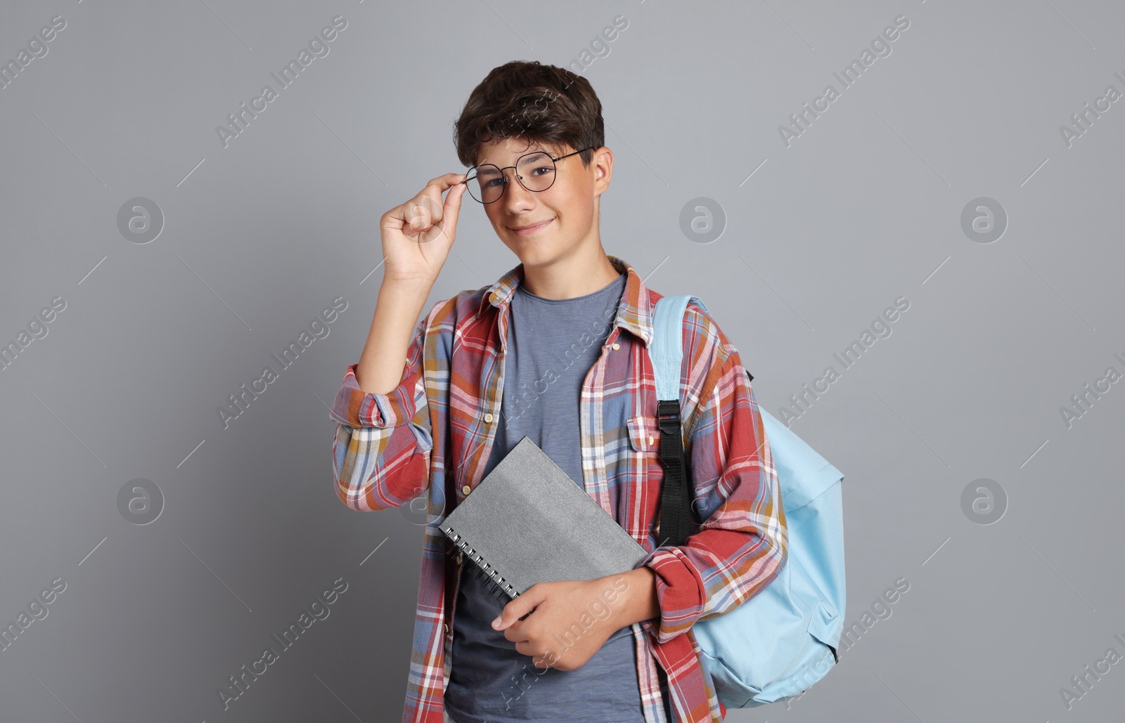 Teenage boy with notebook and backpack on grey background Photo of Teenage boy with notebook and backpack on grey background