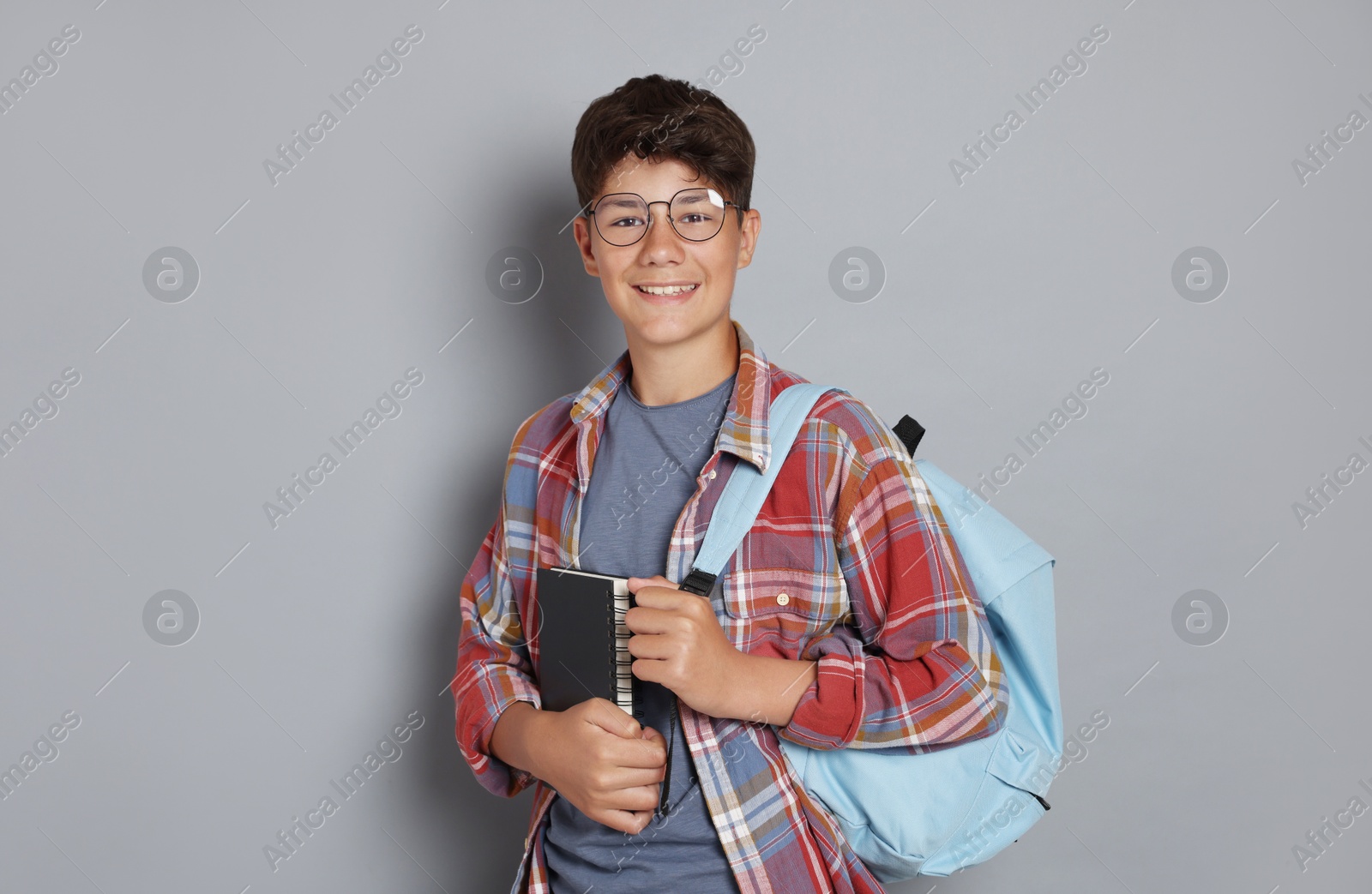 Teenage boy with notebook and backpack on grey background Photo of Teenage boy with notebook and backpack on grey background