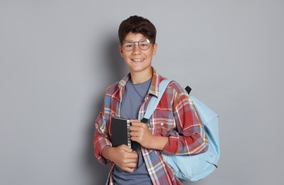 Photo of Teenage boy with notebook and backpack on grey background