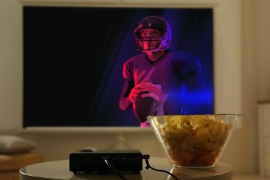 Image of Video projector and bowl with chips on wooden table. Ready to watch sports event