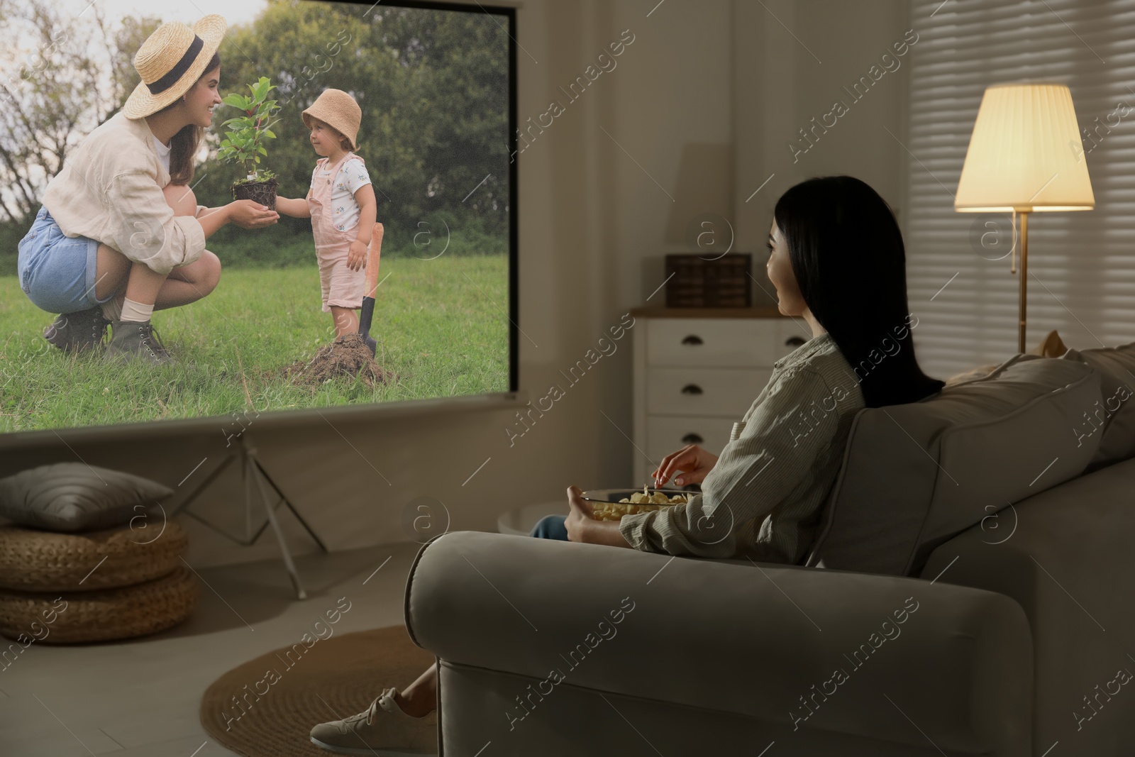 Young woman watching movie using video projector at home Image of Young woman watching movie using video projector at home