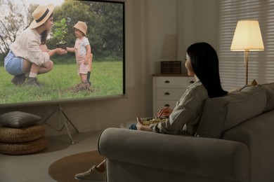 Image of Young woman watching movie using video projector at home