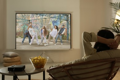 Image of Young woman watching entertainment show using video projector at home