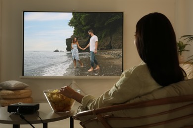 Image of Young woman watching movie using video projector at home