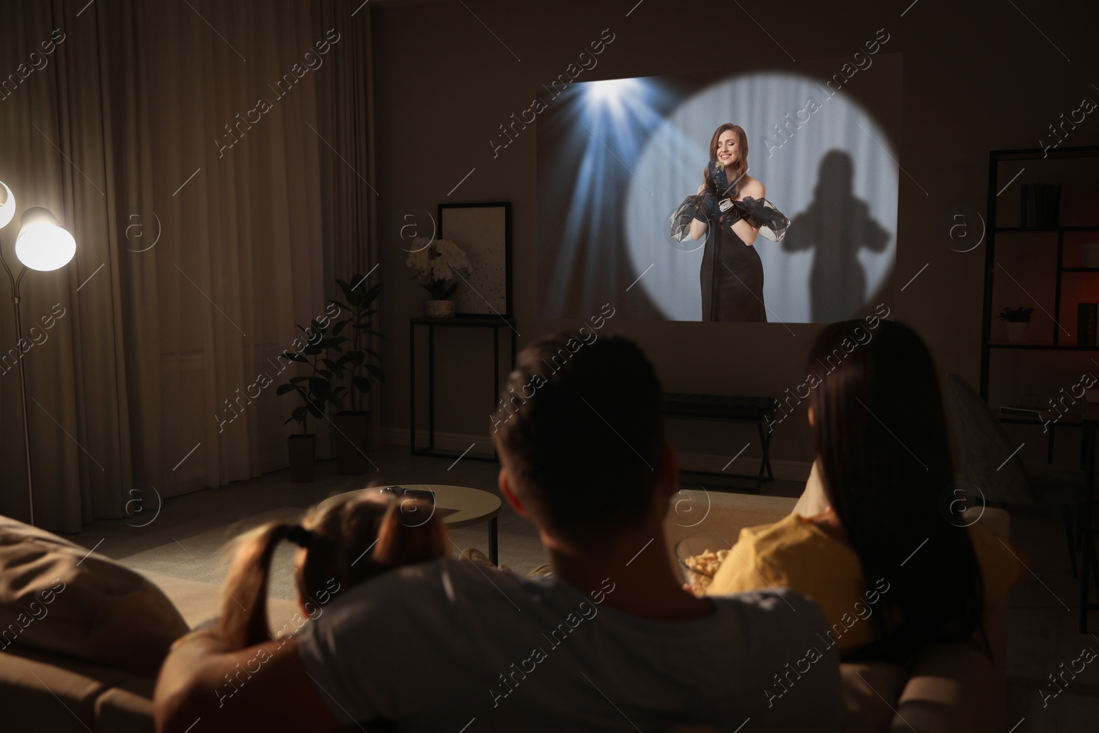 Family watching entertainment show using video projector on sofa at night Image of Family watching entertainment show using video projector on sofa at night