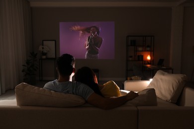 Image of Couple watching entertainment show using video projector on sofa at night