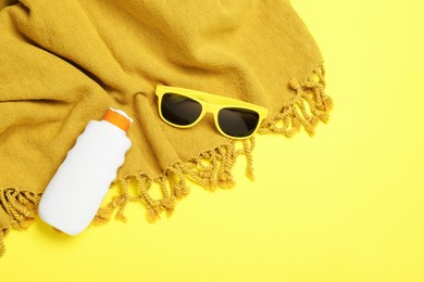 Photo of Beach towel, sunglasses and sunscreen on yellow background, flat lay. Space for text