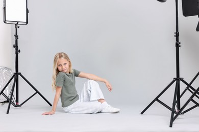 Photo of Little girl on light grey background in photo studio with professional equipment