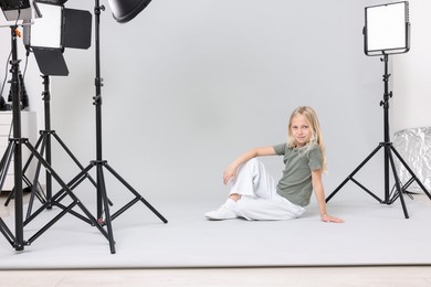 Photo of Little girl on light grey background in photo studio with professional equipment