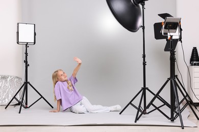 Photo of Little girl on light grey background in photo studio with professional equipment