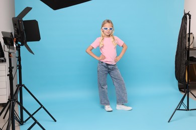 Photo of Little girl on light blue background in photo studio with professional equipment