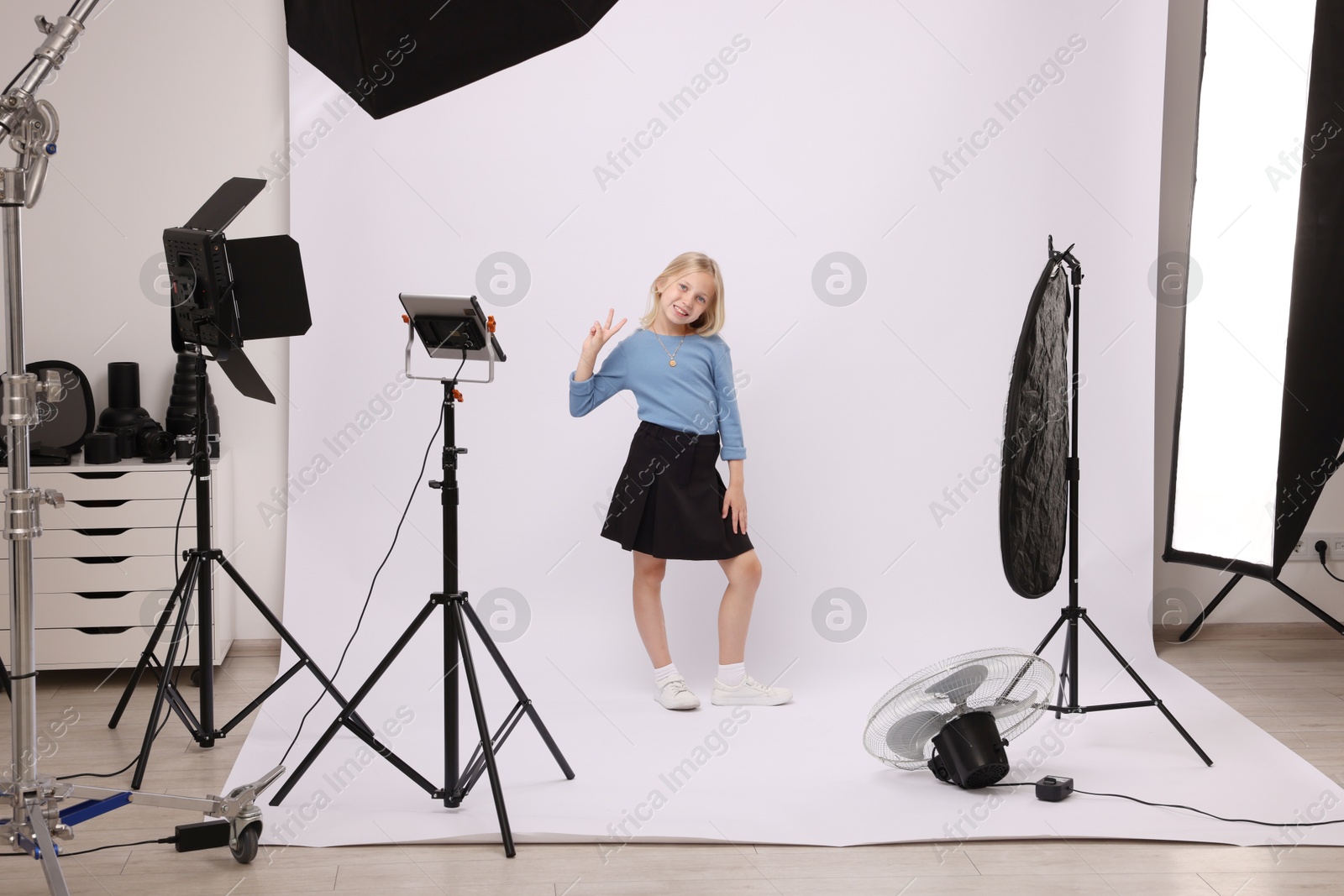 Photo of Little girl showing peace sign on white background in photo studio with professional equipment