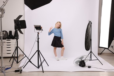 Photo of Little girl showing peace sign on white background in photo studio with professional equipment