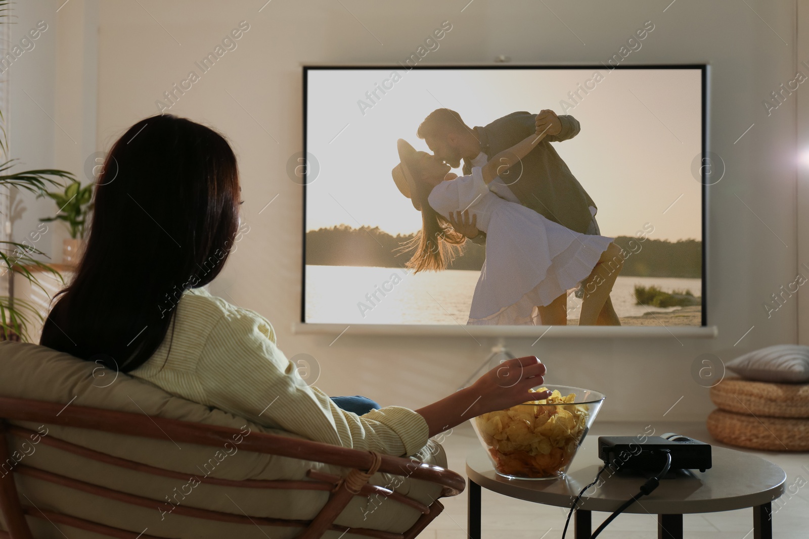 Image of Young woman watching movie using video projector at home