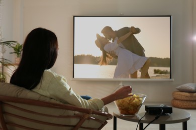 Image of Young woman watching movie using video projector at home