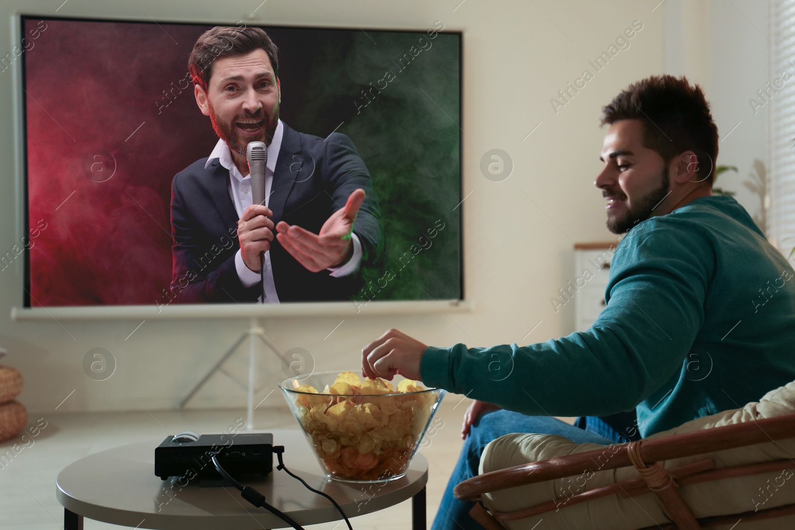 Image of Young man watching entertainment show using video projector at home