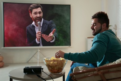 Image of Young man watching entertainment show using video projector at home