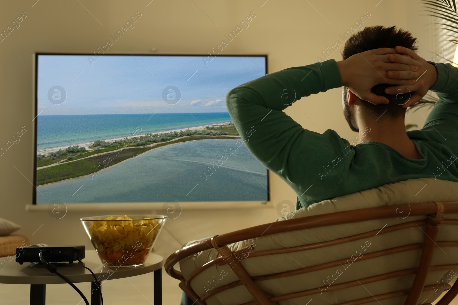 Young man watching travel show using video projector at home Image of Young man watching travel show using video projector at home