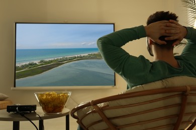 Image of Young man watching travel show using video projector at home