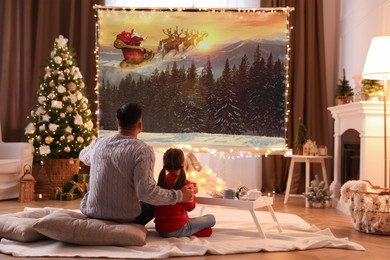 Image of Father and daughter watching Christmas movie using video projector at home