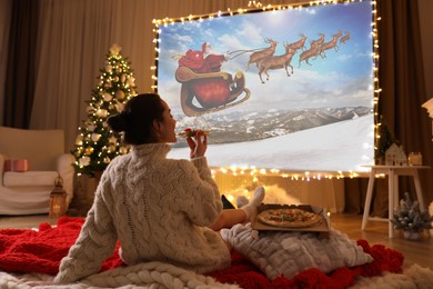 Image of Woman eating pizza and watching Christmas movie using video projector at home