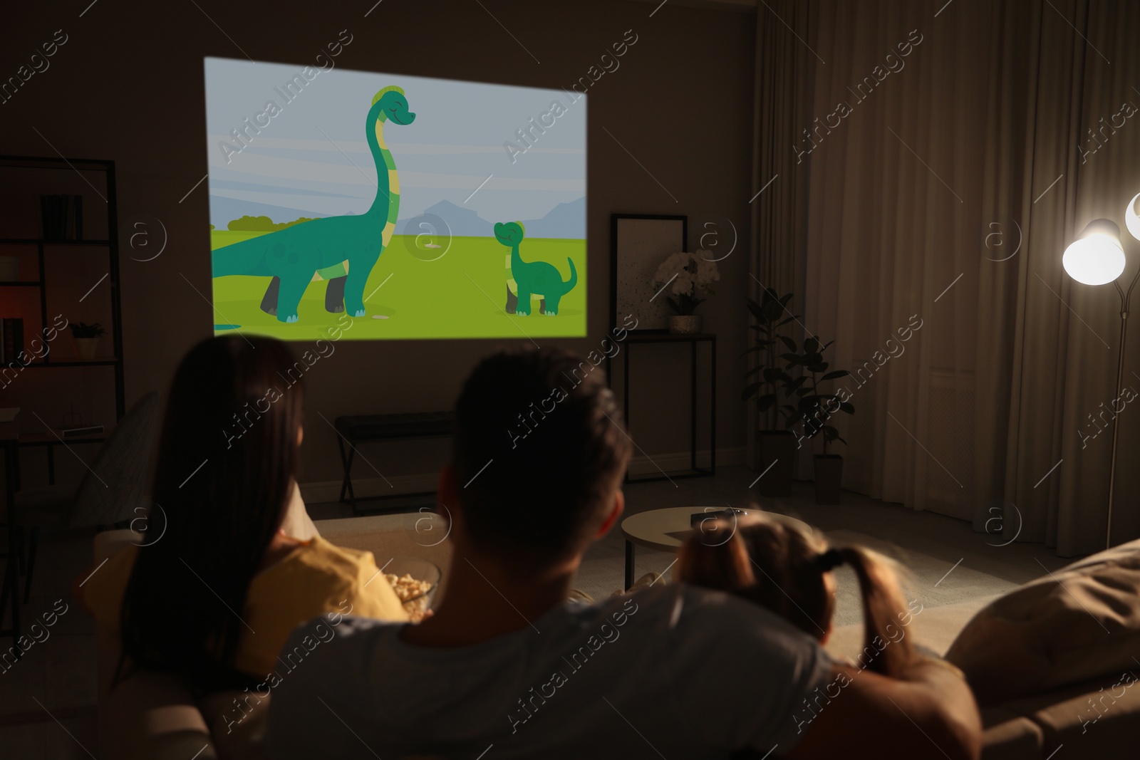 Family watching cartoon using video projector on sofa at night Image of Family watching cartoon using video projector on sofa at night