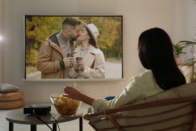 Image of Young woman watching movie using video projector at home