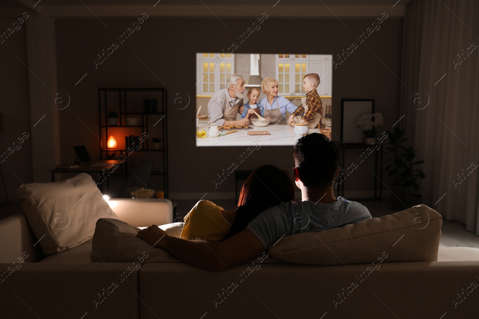 Couple watching movie using video projector on sofa at night Image of Couple watching movie using video projector on sofa at night