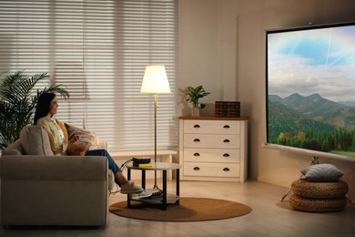Image of Young woman watching travel show using video projector at home