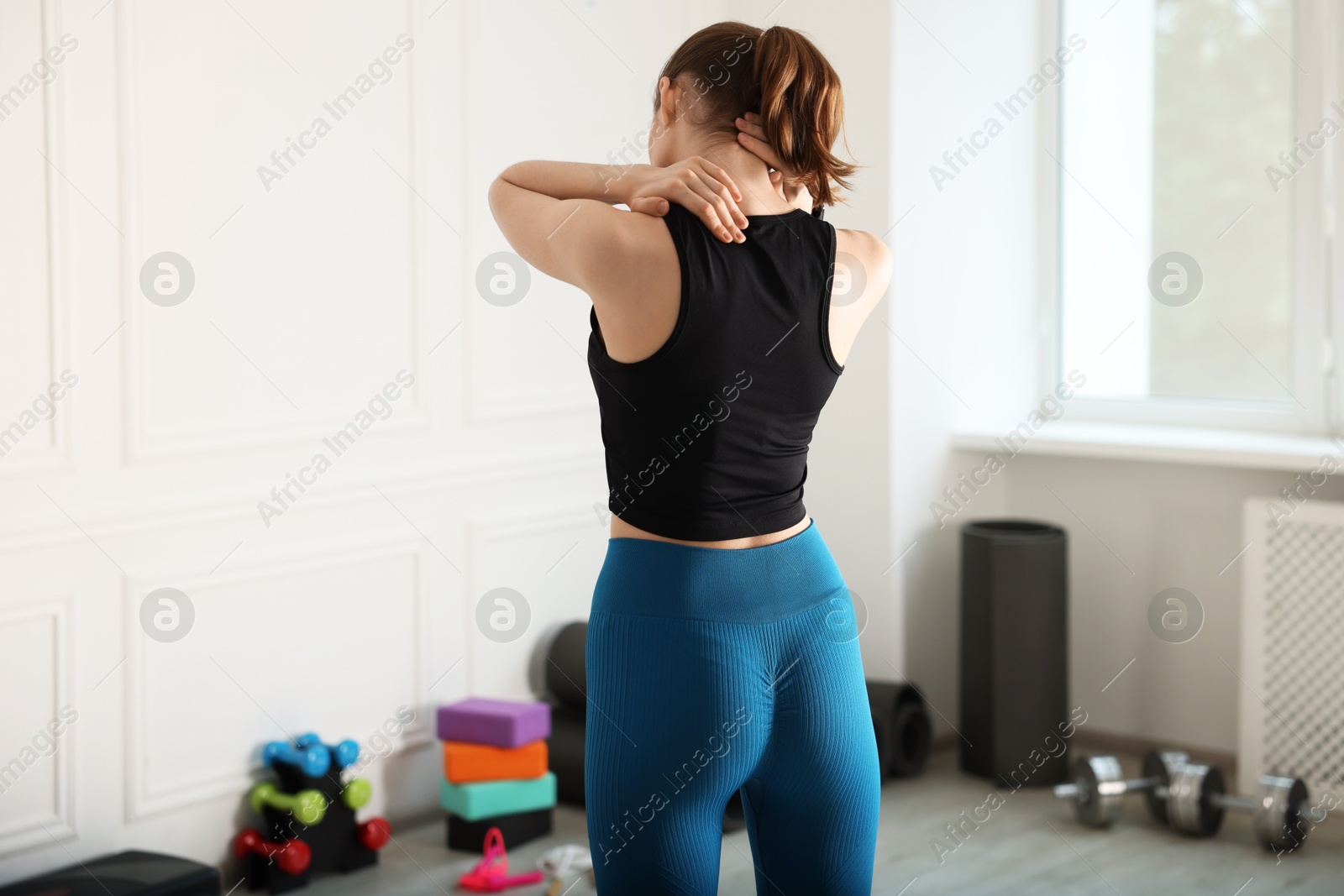 Sports injury. Young woman suffering from shoulder pain in fitness studio, back view Photo of Sports injury. Young woman suffering from shoulder pain in fitness studio, back view