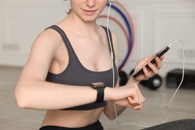 Photo of Woman checking fitness tracker during training indoors, closeup