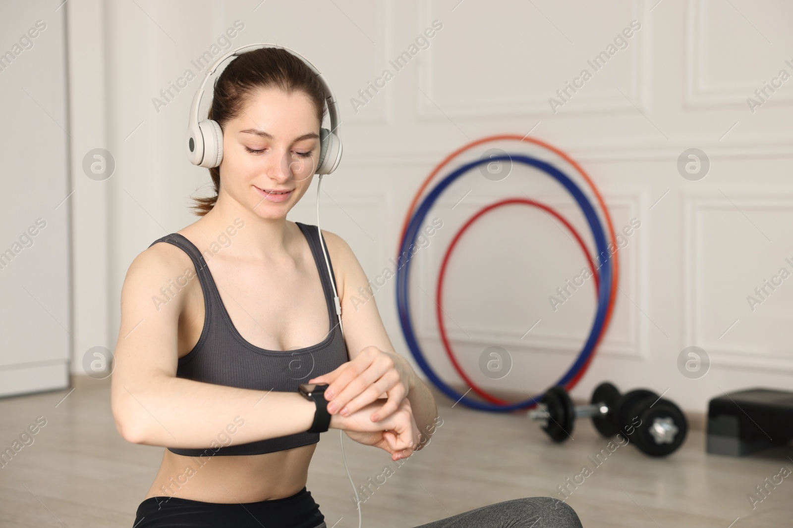 Woman checking fitness tracker during training indoors, space for text Photo of Woman checking fitness tracker during training indoors, space for text