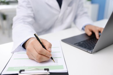 Photo of Doctor using laptop at table in clinic, selective focus. Online medical consultation