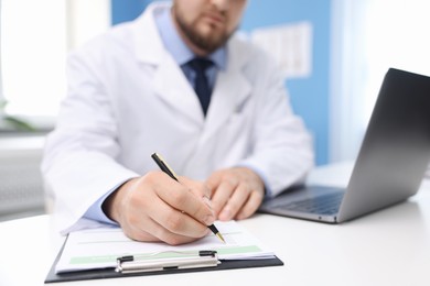 Photo of Doctor working at table with laptop in clinic, selective focus. Online medical consultation