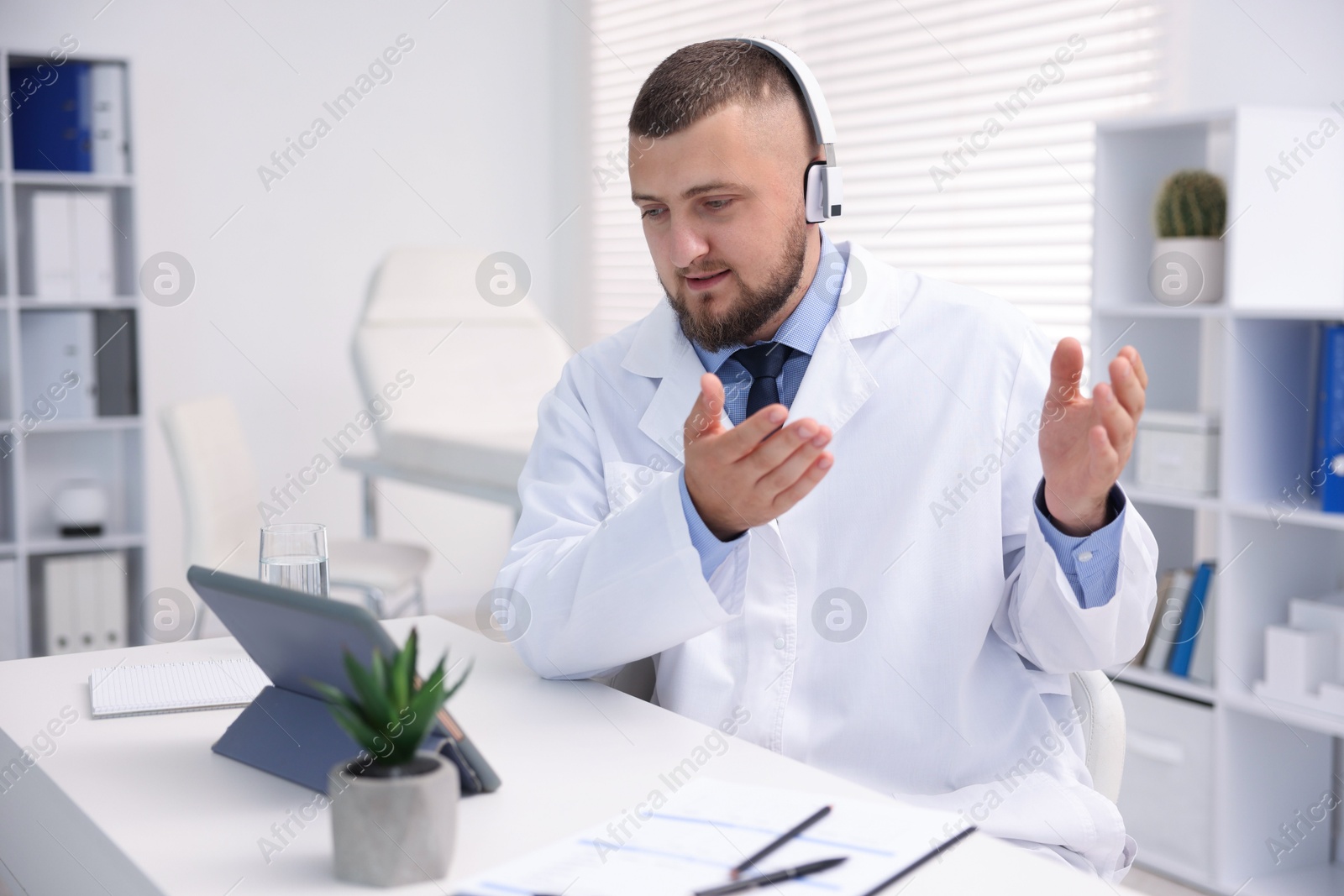 Photo of Doctor in headphones having online consultation via tablet indoors