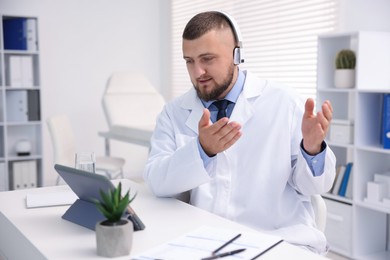 Photo of Doctor in headphones having online consultation via tablet indoors
