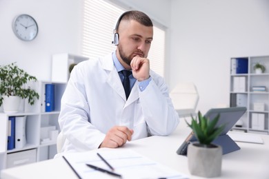 Photo of Doctor in headphones having online consultation via tablet indoors