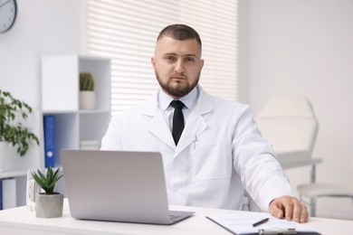 Photo of Doctor working at table with laptop in clinic. Online medical consultation