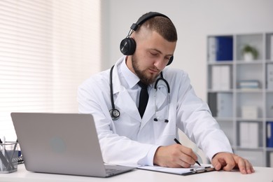 Photo of Doctor in headphones having online consultation via laptop indoors