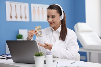Photo of Doctor in headphones with pills having online consultation via laptop indoors