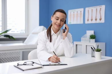 Photo of Doctor with smartphone having online consultation at table in clinic